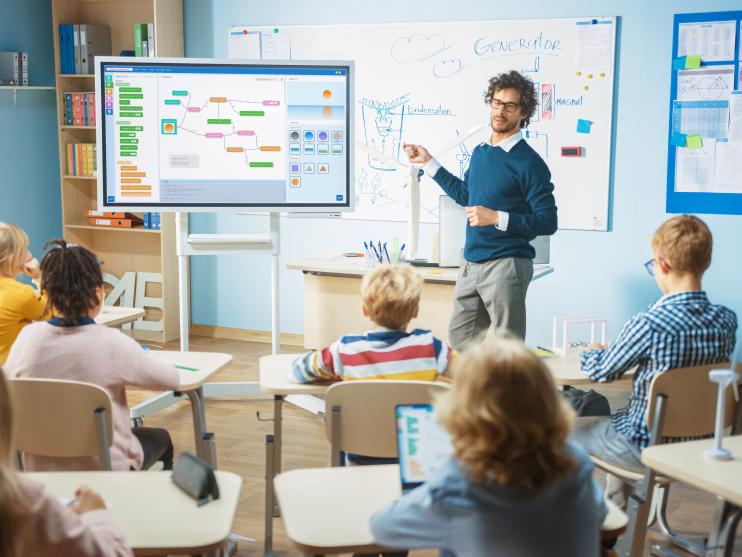 Lehrer an digitalem Whiteboard vor Schulklasse