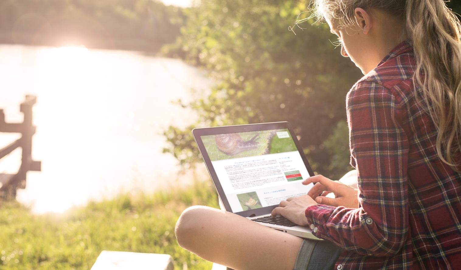 Eine Person sitzt mit einem Laptop an einem See und schaut sich das neue Datenportal "Mollusken Deutschlands" an 