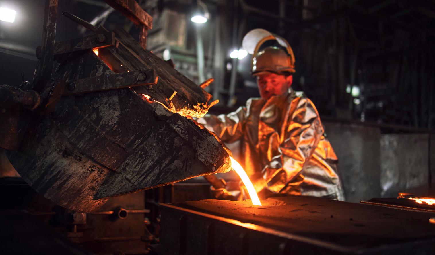 Ein Gießereiarbeiter gießt heißes flüssiges Eisen in Formen.