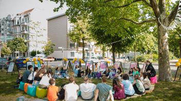 Jugendliche und zwei Betreuer sitzen auf einer Wiese und arbeiten an einem Projekt