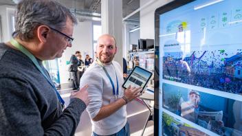 Zwei Personen stehen bei einer Ausstellung vor einem Bildschirm mit Nachrichten