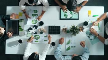 Geschäftsteam, das an einem Besprechungstisch mit Windrad über die Nutzung sauberer Energie und nachhaltige Investitionen diskutiert.