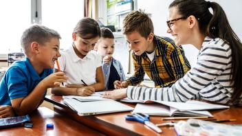 Schüler sitzen an einem Tisch mit einer Lehrerin
