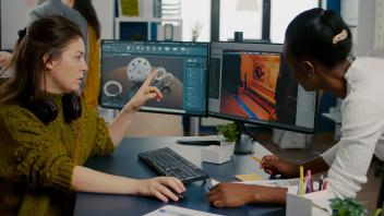 Zwei Mitarbeitende entwickeln das Design eines Spiels mithilfe eines PCs mit zwei Monitoren