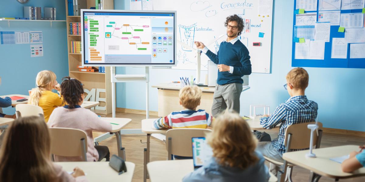 Lehrer an digitalem Whiteboard vor Schulklasse