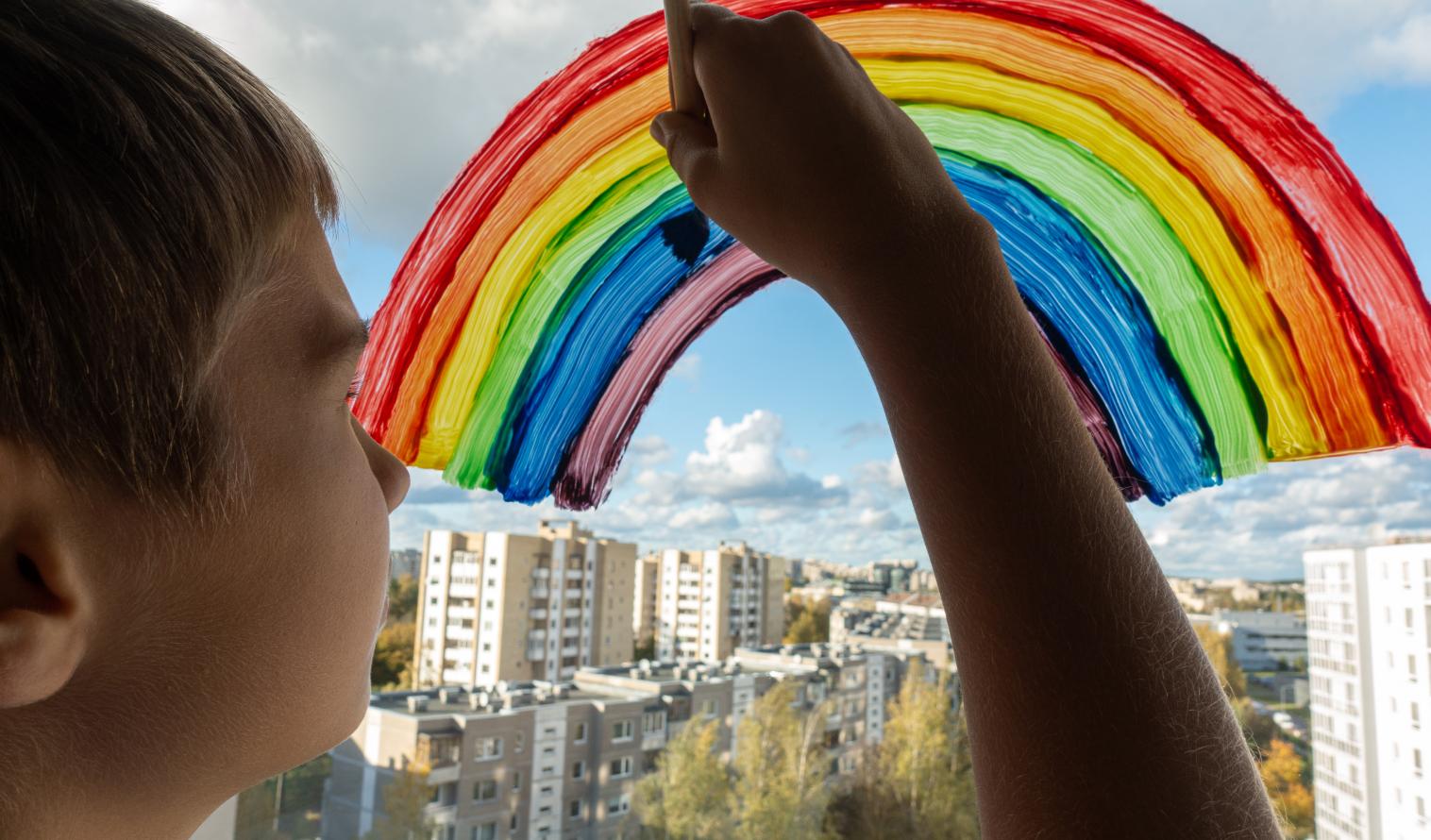 Kind malt einen Regenbogen auf ein Fenster