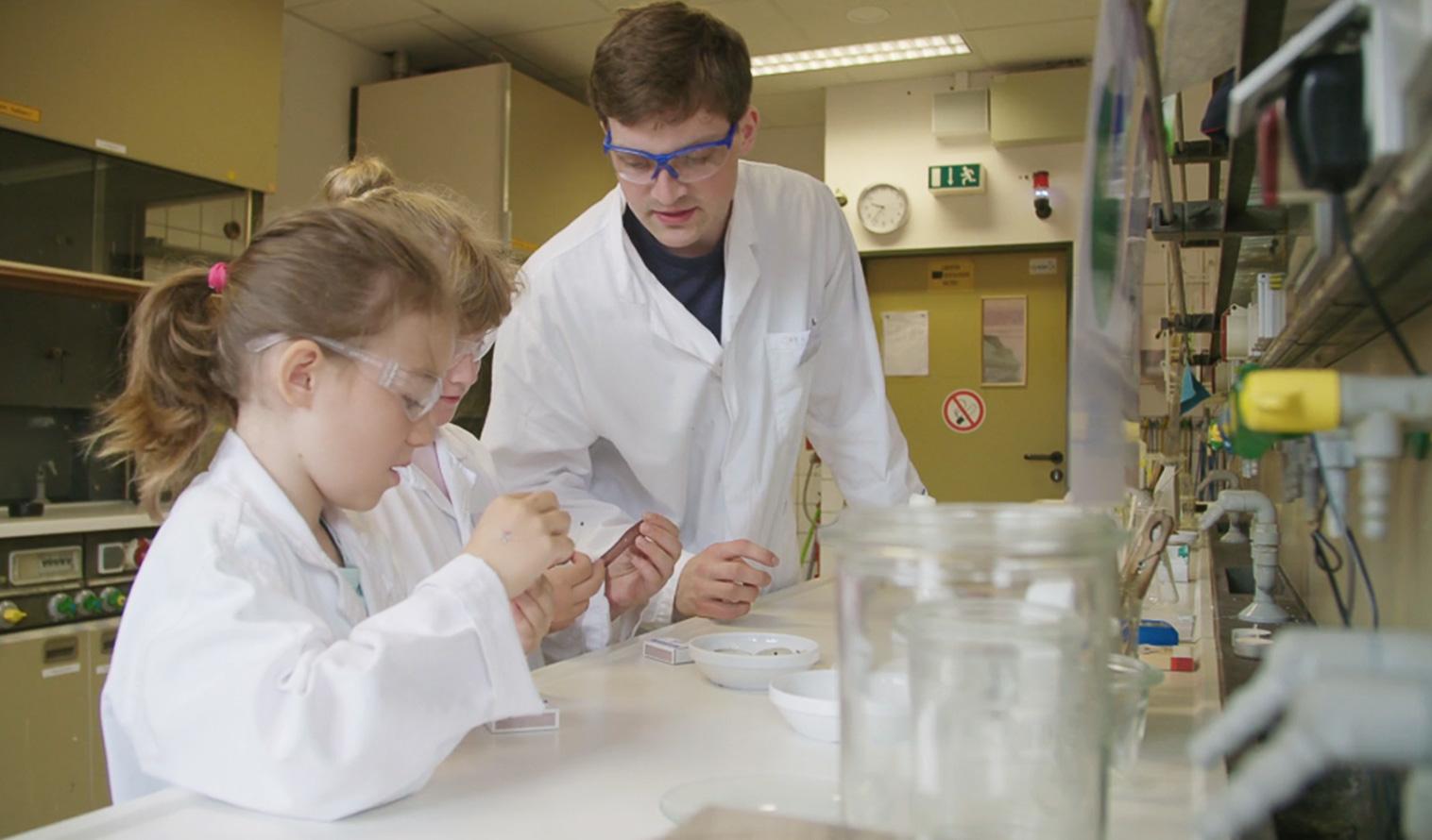 Ein Lehrer bereitet mit zwei Schülerinnen ein Experiment in einem Labor vor.