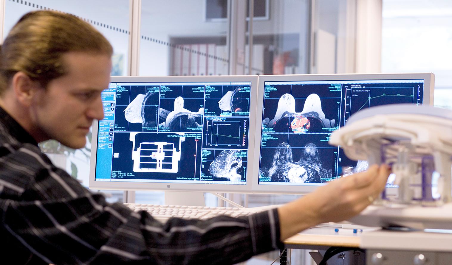 Eine Person sitzt vor zwei Monitoren, die Mammographien zeigen.