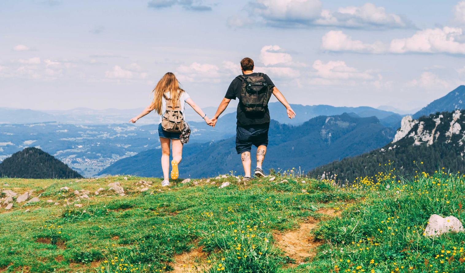 Man und Frau laufen Hand in Hand über eine Bergwiese