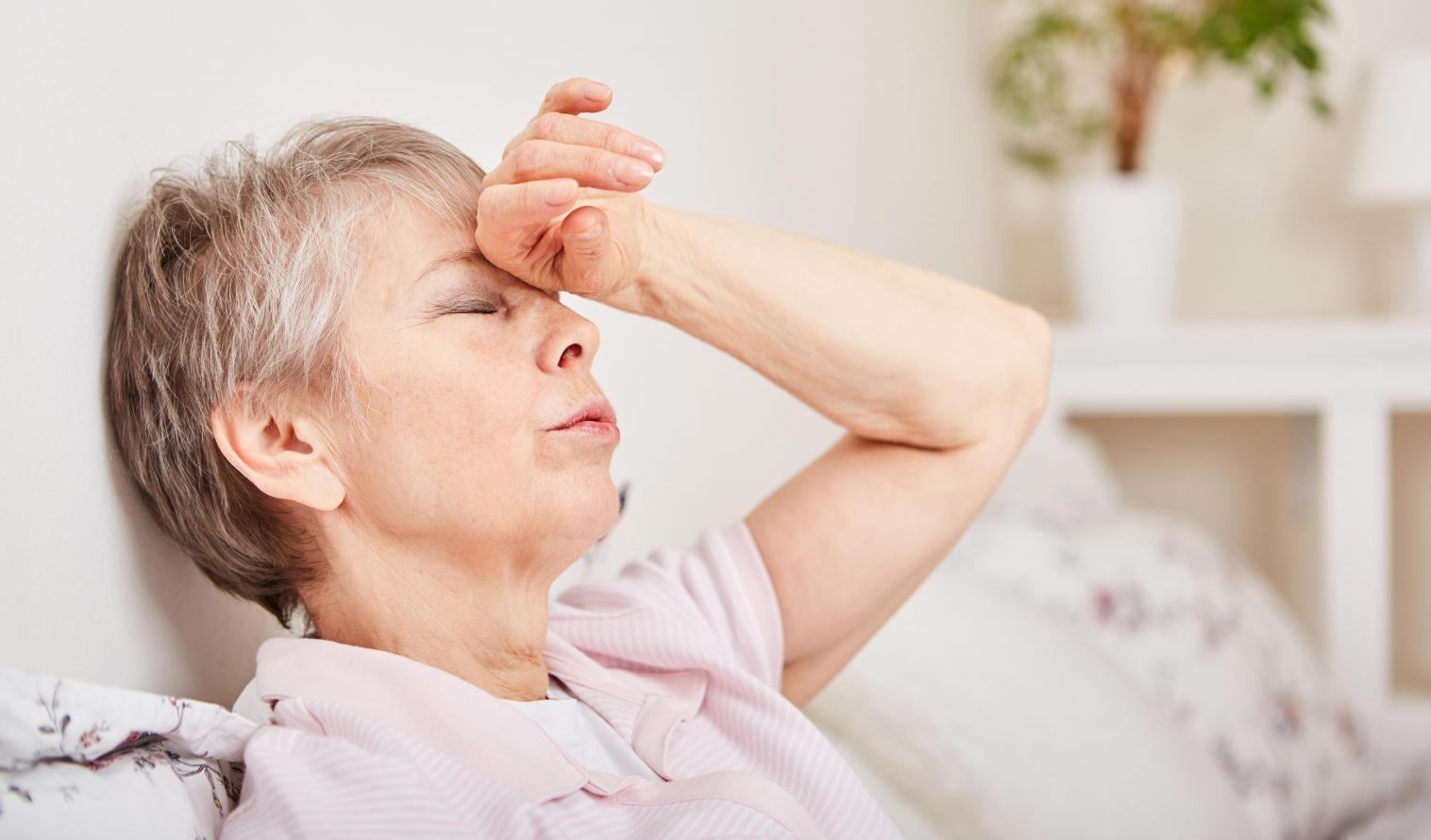 Seniorin mit Kopfschmerzen liegt im Bett