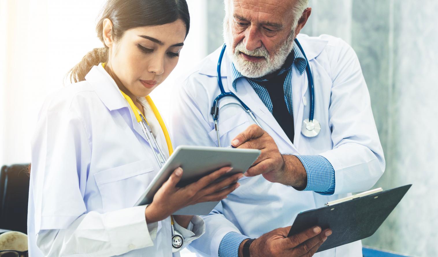 Ein älterer Arzt und eine junge Ärztin mit einem Tablet in der Hand unterhalten sich