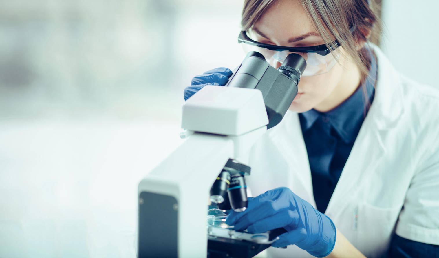 Wissenschaftlerin schaut durch ein Mikroskop in einem Labor