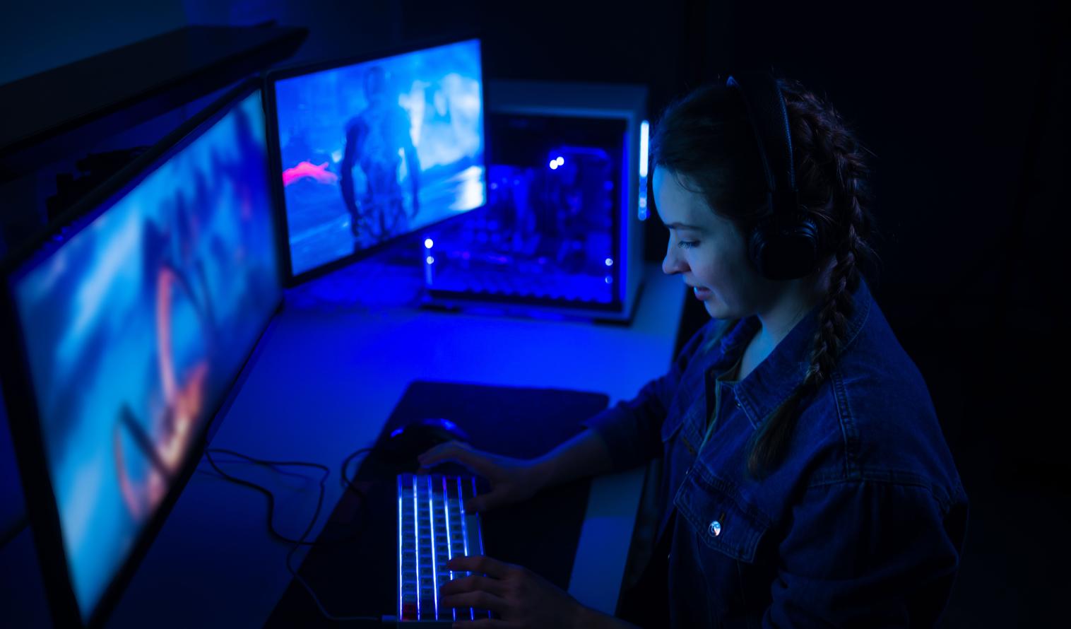 Frau mit Kopfhörern spielt ein Computerspiel auf großen Monitoren