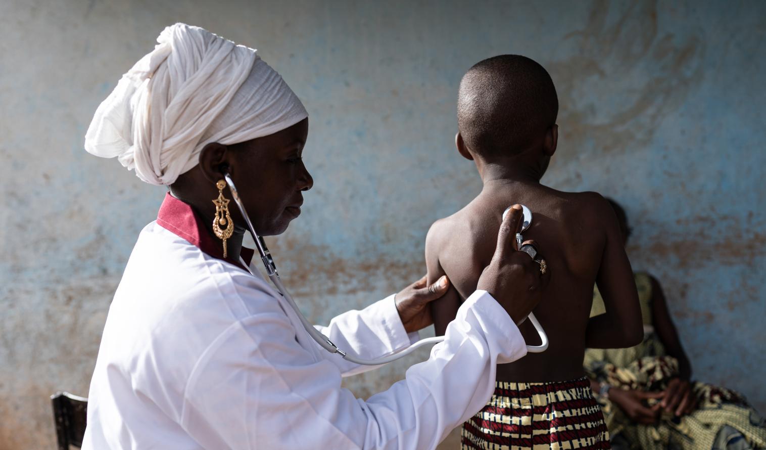 Arzt in weißer Uniform, der mit einem Stethoskop die Lungentöne eines kleinen Jungen abhört