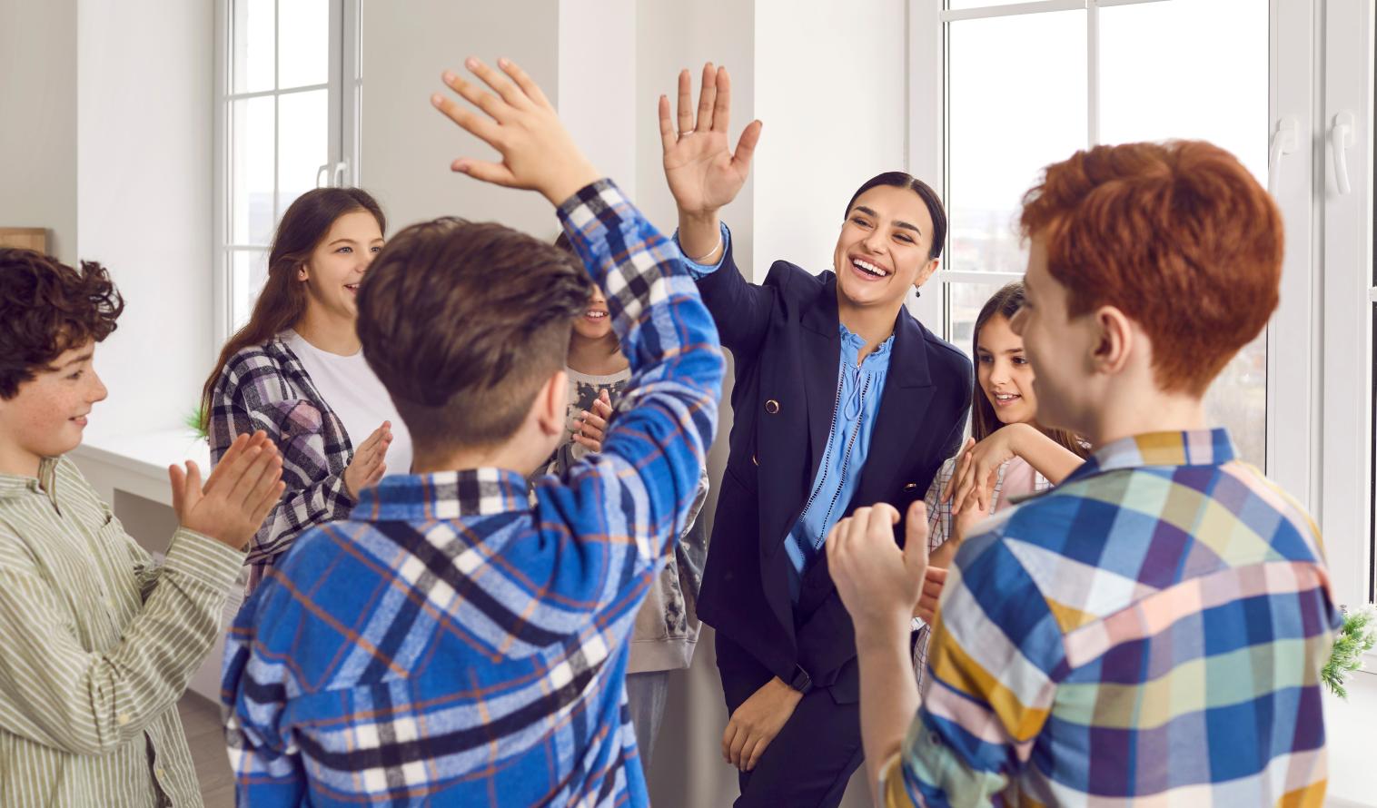 Eine Lehrerin gibt einem Schüler ein High Five, während andere in die Hände klatschen. 