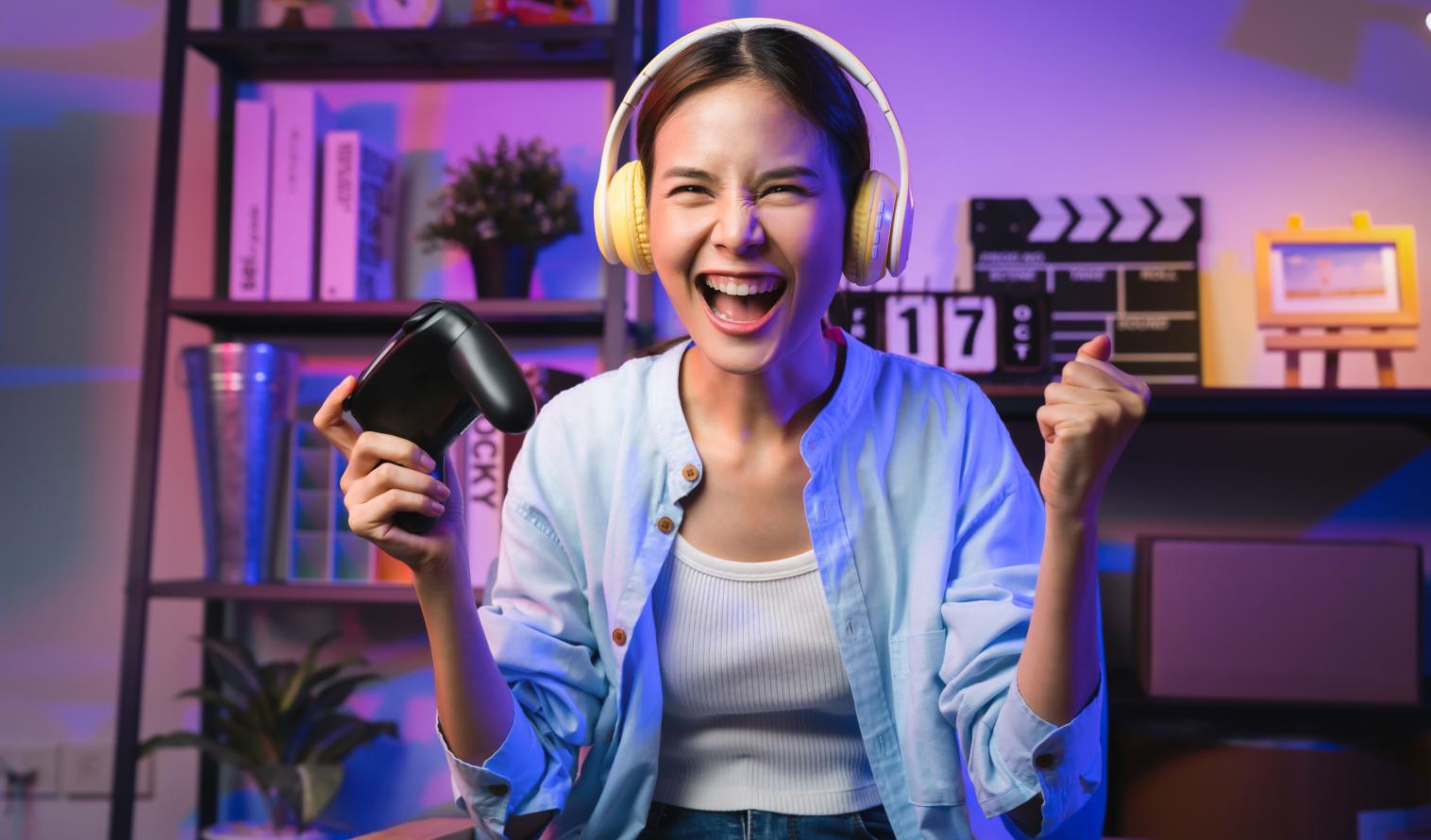 Aufgeregte junge Frau mit Kopfhörern hält einen Spiele-Controller in der Hand 