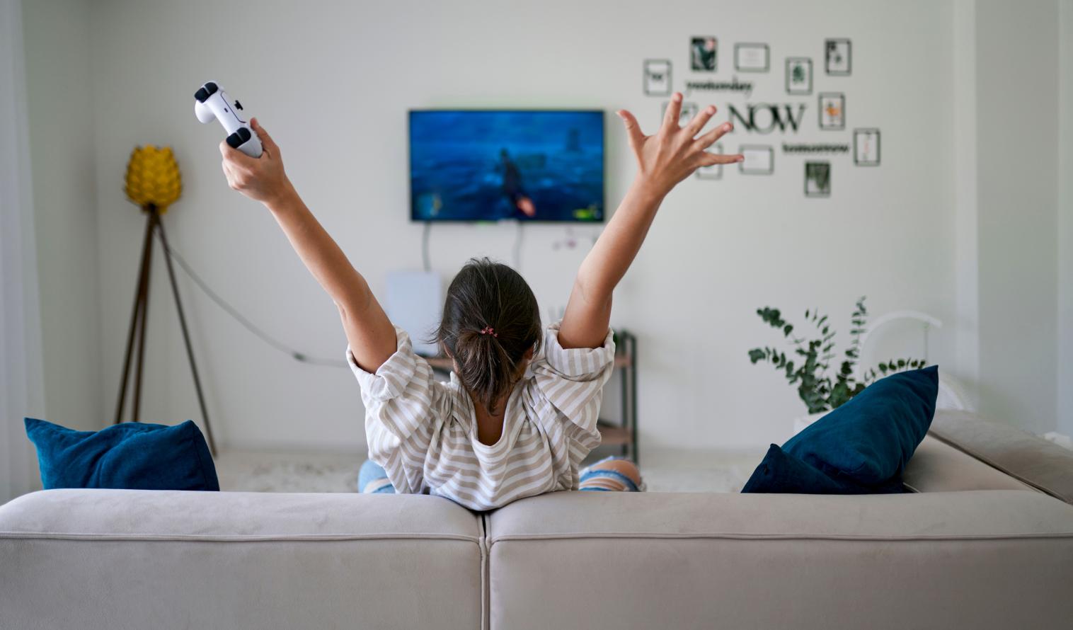 Frau gewinnt in einem Computerspiel und sitzt mit erhobenen Armen zu Hause