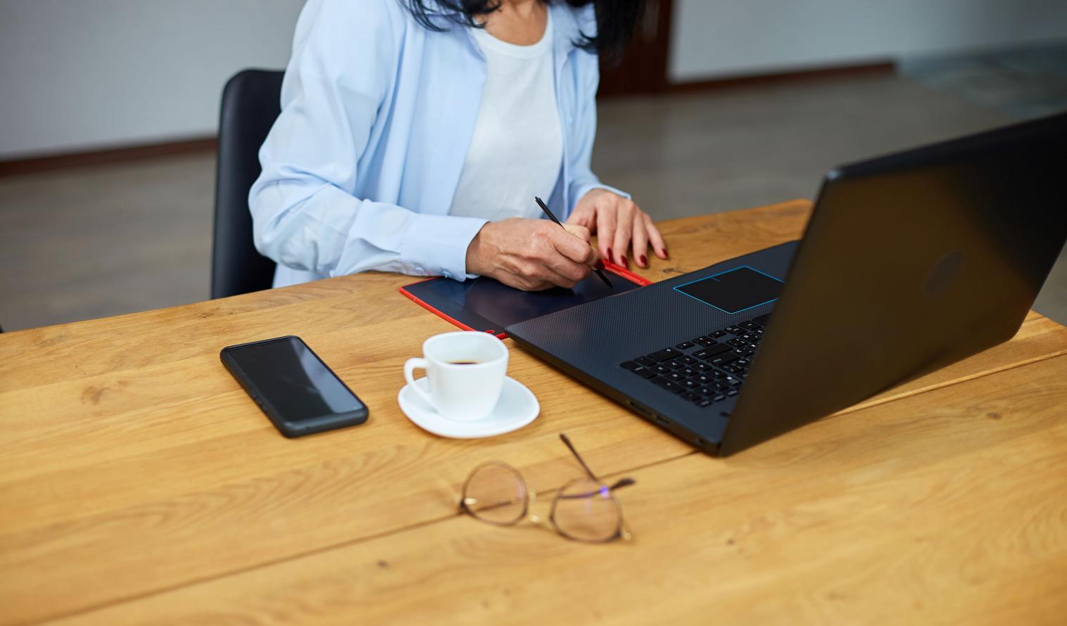 Eine Frau sitzt an einem Schreibtisch mit einem Tablet und einem Laptop