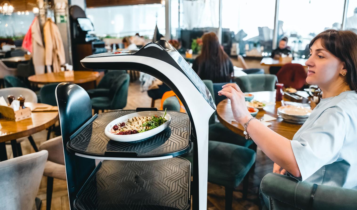 Roboter-Kellner serviert einer Frau Essen in einem modernen Restaurant.