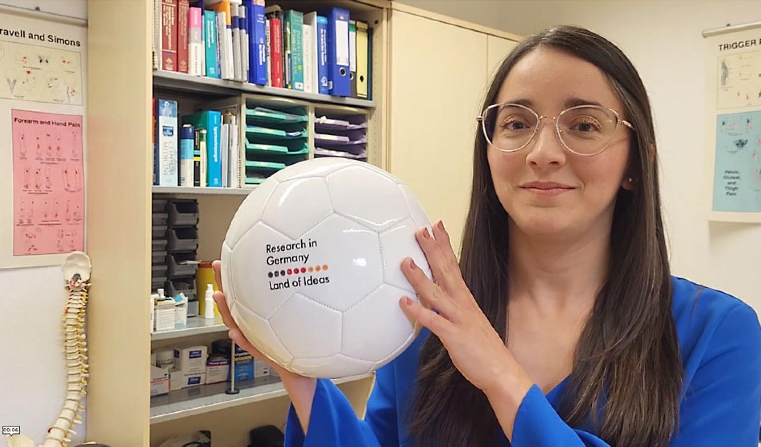 Wissenschaftlerin Monica Duarte Muñoz hält einen Fussball mit der Aufschrift Research in Germany Land of ideas in der Hand.