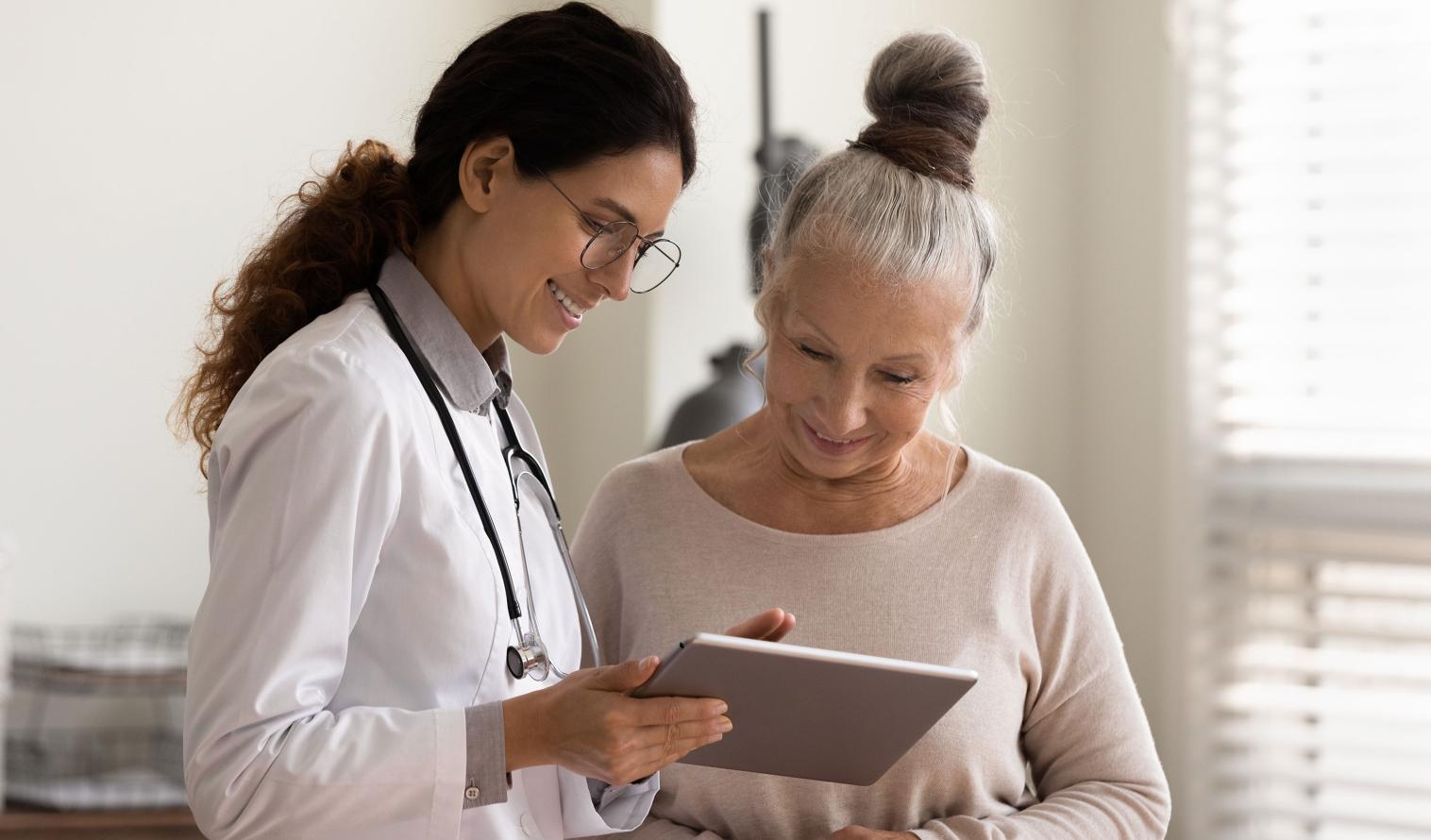 Eine Ärztin hält ein Tablet in der Hand und erklärt einer älteren Patientin etwas