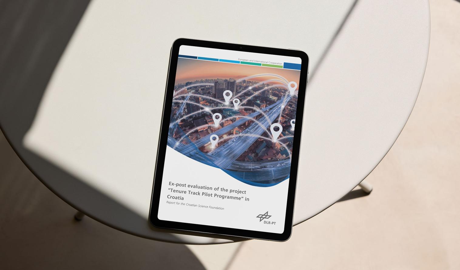 ein Tablet liegt auf einem Glastisch, die erste Seite des Evaluationsbericht des Tenure-Track-Pilotprogramms wird darauf angezeigt