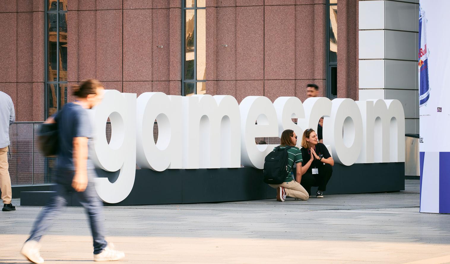 Personen sitzen vor einem Gamescom Logo auf dem Messegelände in Köln