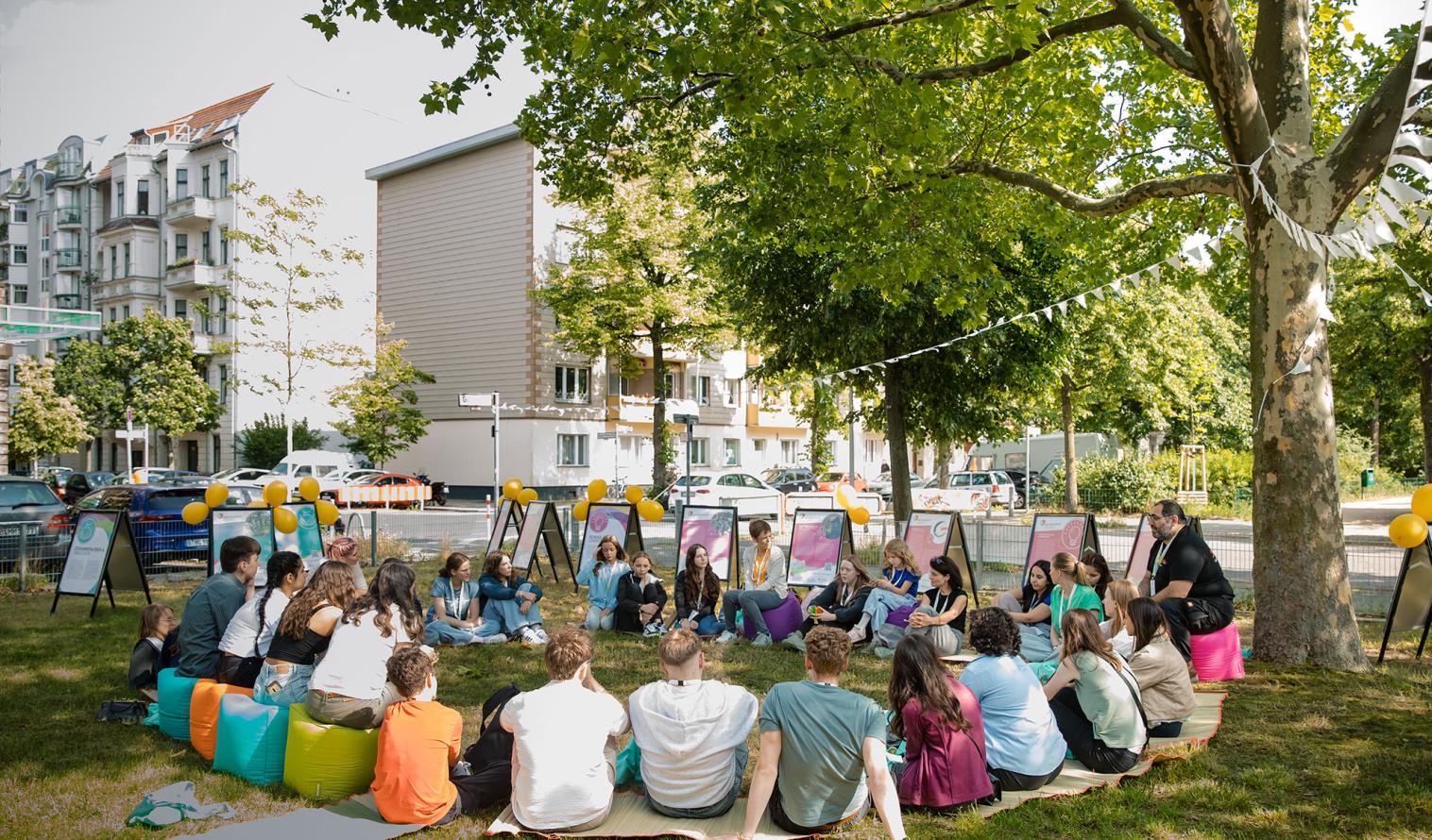 Jugendliche und zwei Betreuer sitzen auf einer Wiese und arbeiten an einem Projekt