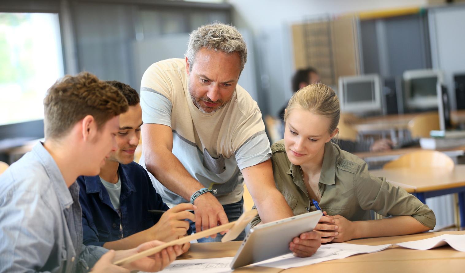 Lehrer arbeitet mit einer Gruppe von Studierenden auf einem Tablet 