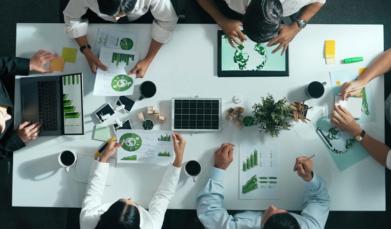 Geschäftsteam, das an einem Besprechungstisch mit Windrad über die Nutzung sauberer Energie diskutiert.