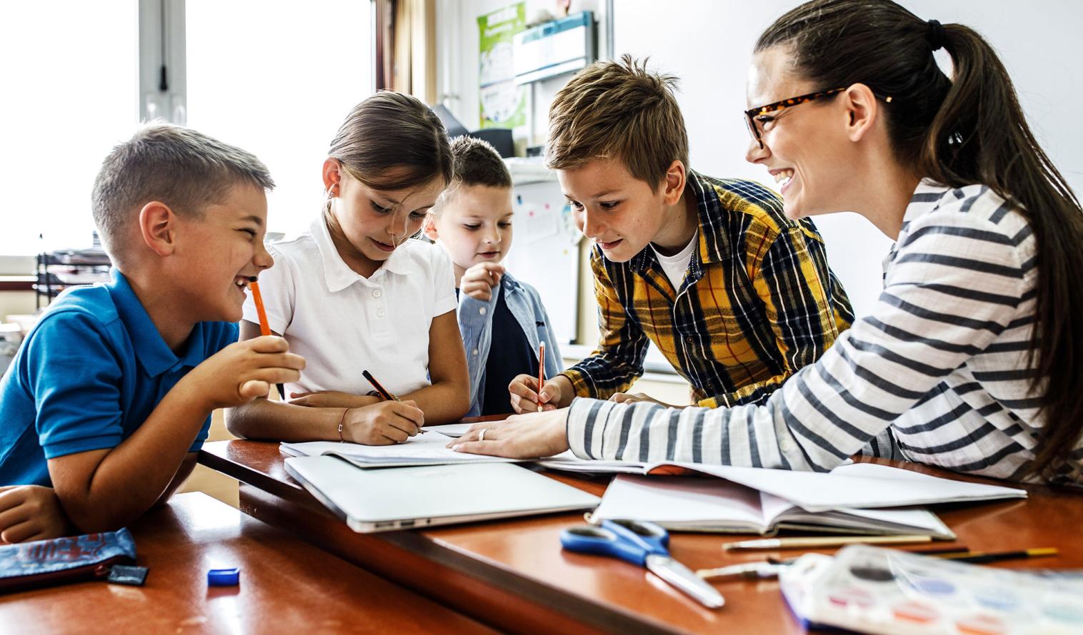 Schüler sitzen an einem Tisch mit einer Lehrerin