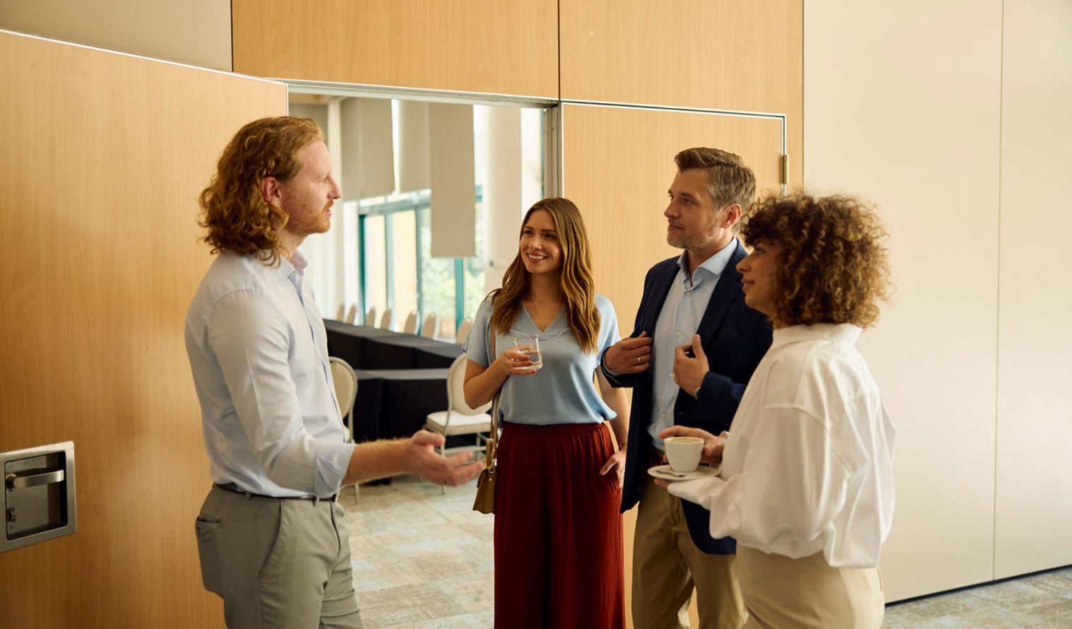 vier Personen führen vor einem Veranstaltungsraum ein Gespräch