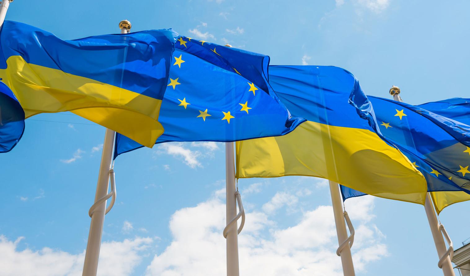 Eine Reihe von Fahnenmasten, an denen die Flaggen der Europäischen Union und der Ukraine vor dem Hintergrund eines blauen Himmels im Wind wehen