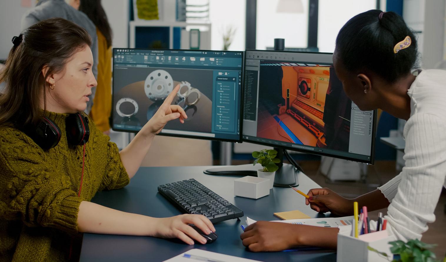 Two staff members are developing the design of a game using a PC with two monitors