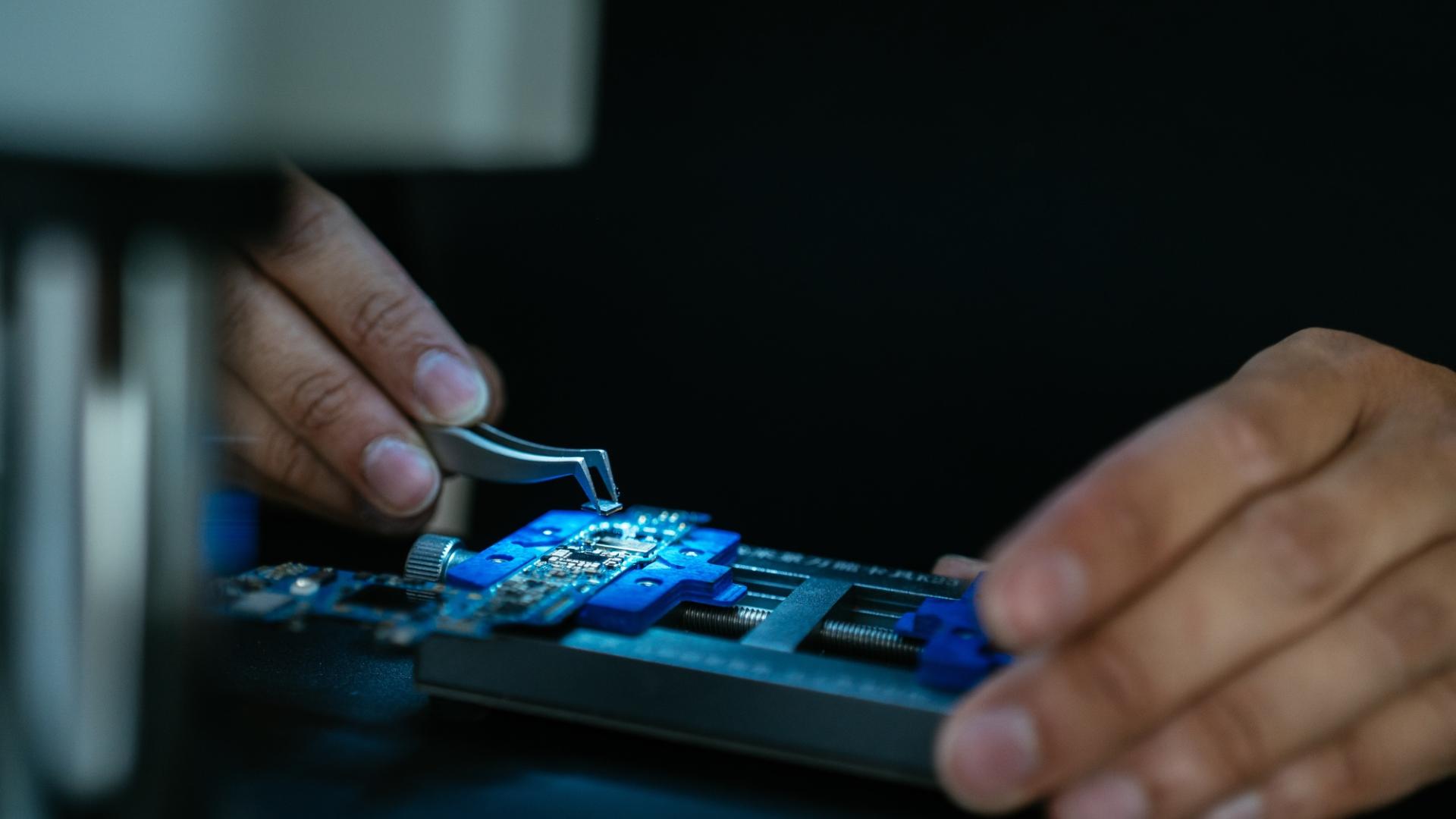 Mensch arbeitet mit Pinzette an einem Computerchip