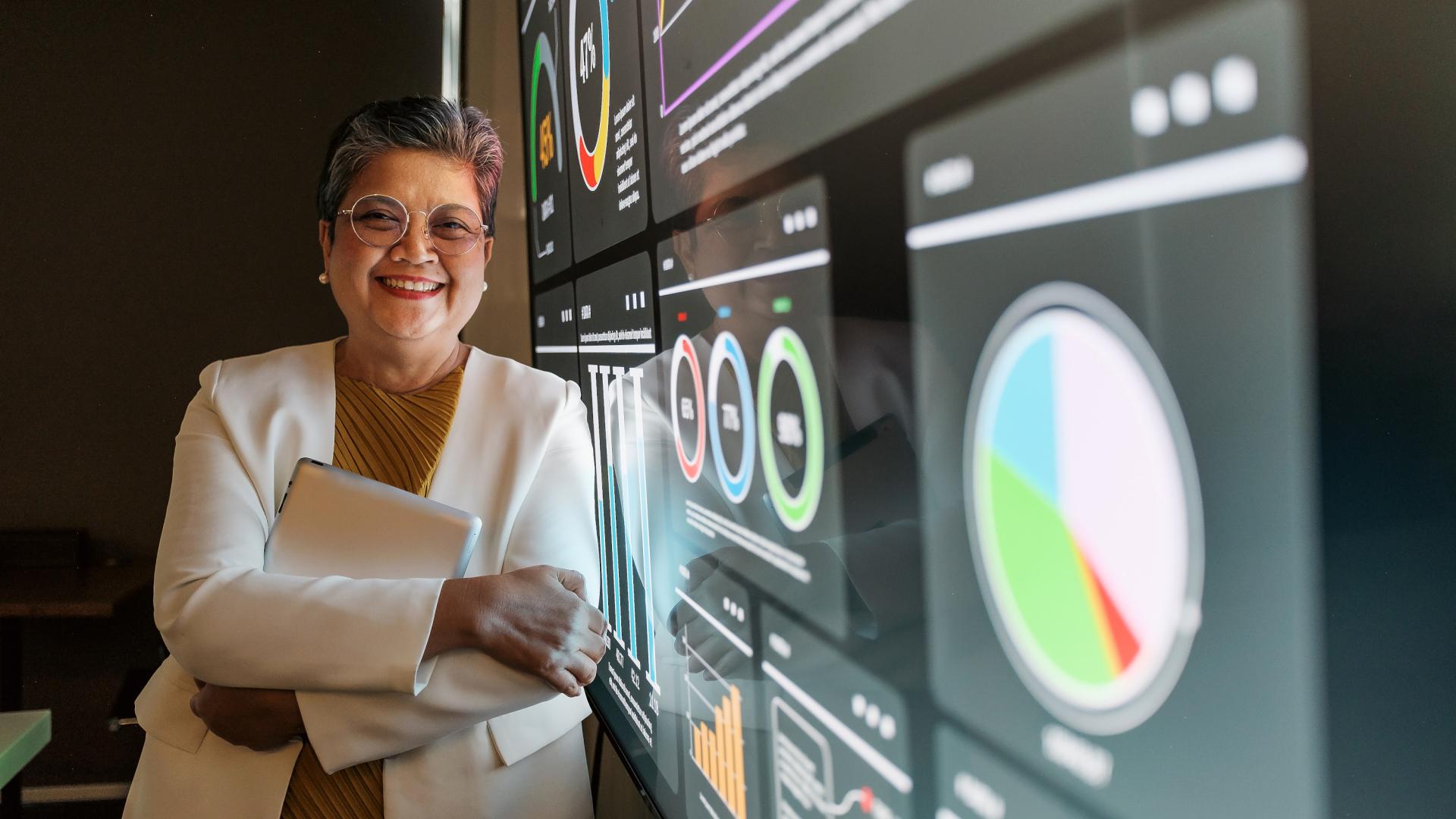 Lächelnde Frau im weißen Anzug steht neben einem digitalen Dashboard